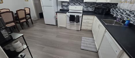 Une cuisine de taille réduite avec des meubles blancs, un plan de travail noir et un pare-feu en carreaux.