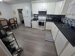 A compact kitchen with white cabinets, a black countertop, and a tiled backsplash.
