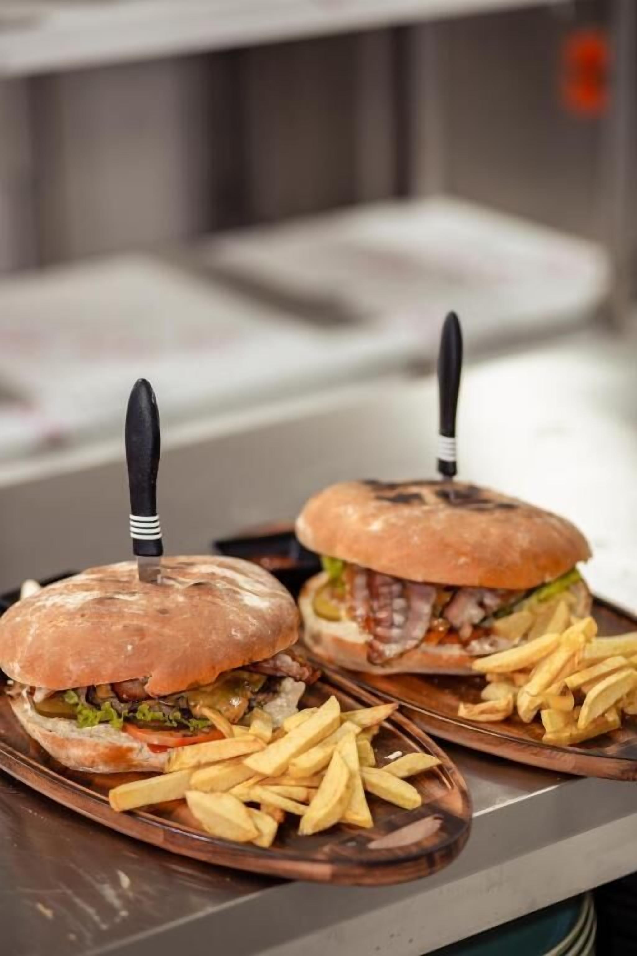 Zwei Burger mit Messer-Spießen auf einer Platte, dazu Pommes.