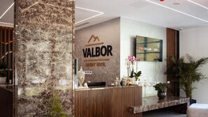 Un mostrador de recepción con una columna de mármol, un mostrador de madera y un televisor montado en la pared.