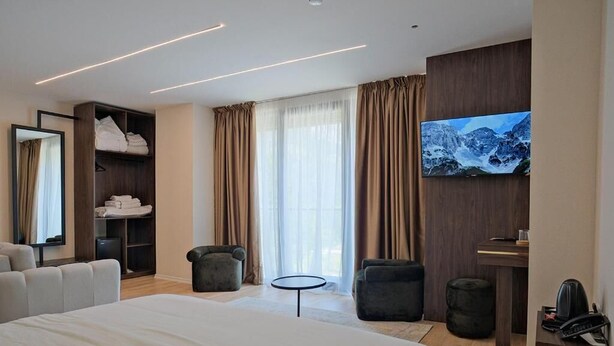 Habitación de hotel con una cama grande, una zona de estar con sillas, una mesita, un armario, un televisor y un escritorio con teléfono.