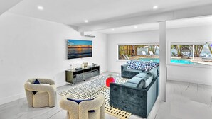 A modern living room with a pool view, a sofa, a coffee table, and a TV. - Hollywood Hills Oasis Pool 7BR Retreat (Hollywood)