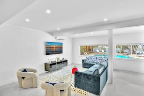 A modern living room with a pool view, a sofa, a coffee table, and a TV. - Hollywood Hills Oasis Pool 7BR Retreat (Hollywood)