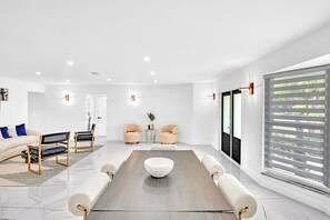 A modern conference room with a long table, two chairs, a sofa, and a large window with blinds.