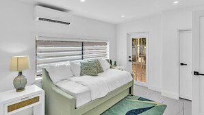 A bedroom with a bed, a bedside table, a lamp, a window with blinds, and a door leading to an outdoor area. - Hollywood Hills Oasis Pool 7BR Retreat (Hollywood)