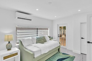 A bedroom with a bed, a bedside table, a lamp, a window with blinds, and a door leading to an outdoor area. - Hollywood Hills Oasis Pool 7BR Retreat (Hollywood)