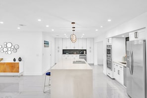 A modern kitchen with white cabinetry, a central island, stainless steel appliances, and a minimalist design. - Hollywood Hills Oasis Pool 7BR Retreat (Hollywood)
