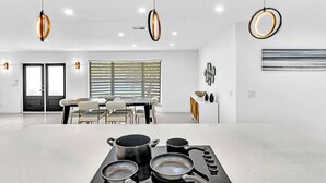 A modern kitchen with a gas stove, pots, and pans, a dining area with a table and chairs, and pendant lighting. - Hollywood Hills Oasis Pool 7BR Retreat (Hollywood)