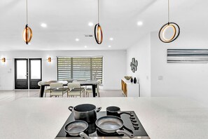 A modern kitchen with a gas stove, pots, and pans, a dining area with a table and chairs, and pendant lighting. - Hollywood Hills Oasis Pool 7BR Retreat (Hollywood)
