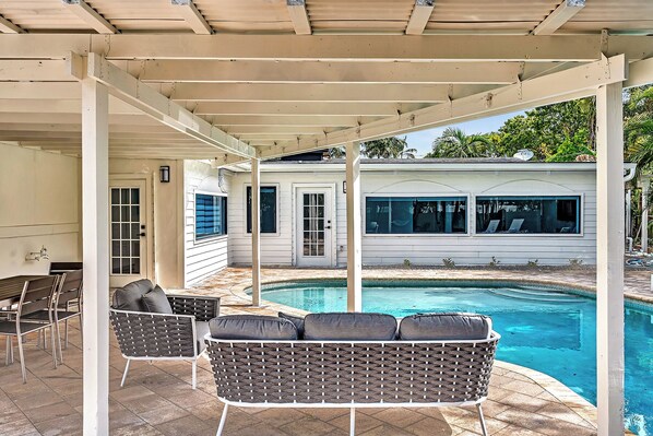 A covered outdoor area with a pool, seating, and a building with windows.