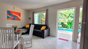 A modern living room with a glass table, white chairs, a black sofa with yellow cushions, and a colorful abstract painting on the wall. - Cozy 1-bedroom Apartment 3 km From Eagle Beach (Noord)