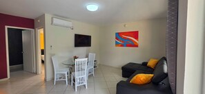 Ein Wohnzimmer mit einer schwarzen Couch, weißen Sesseln, einem Fernseher und einem Gemälde.