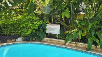 A pool with a sign listing pool and whirlpool rules, surrounded by lush greenery.