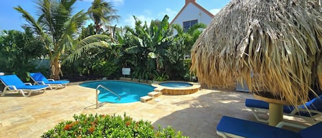 A pool area with lounge chairs, a hot tub, and tropical vegetation.