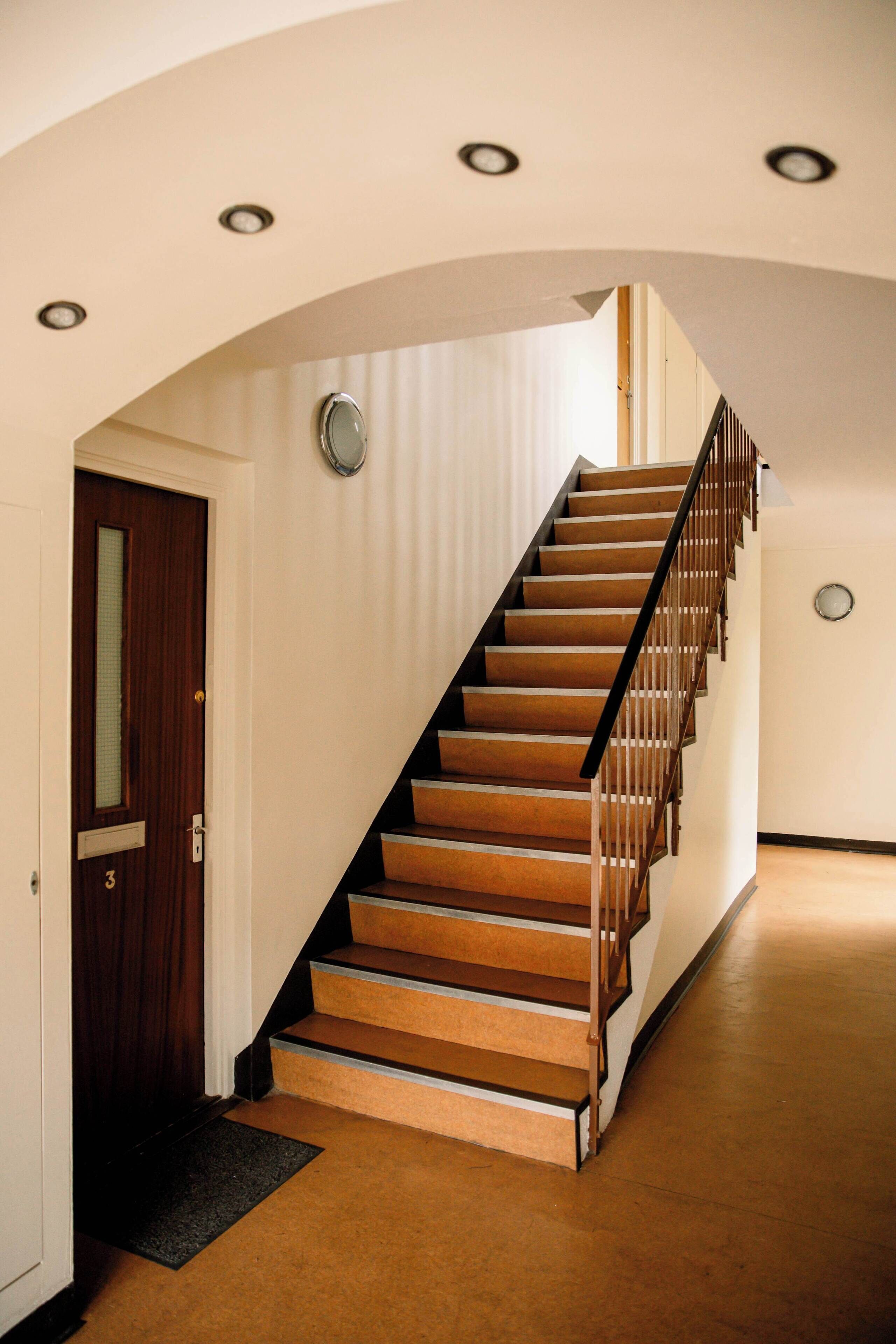 A staircase with wooden steps and a metal railing, leading to a landing with a door and a light fixture.
