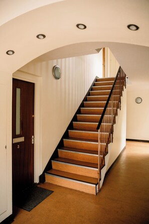 A staircase with wooden steps and a metal railing, leading to a landing with a door and a light fixture. - Homely 3 Bed with Private Parking off Leith Walk (Edinburgh)