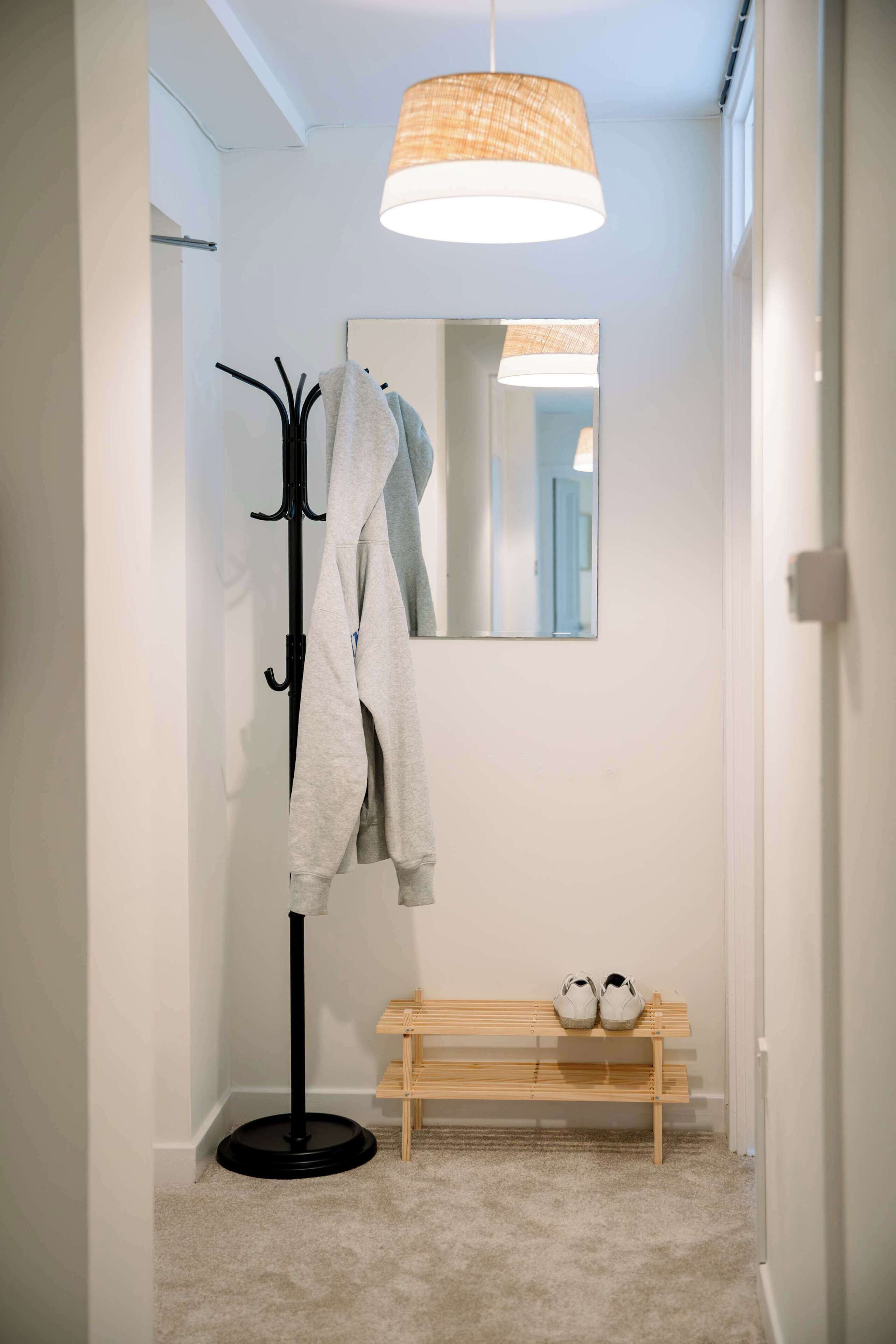 Un corridoio con un appendiabiti, uno specchio, una panca con scarpe e un lampadario.