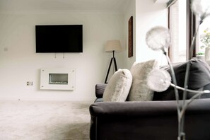 Ein modernes Wohnzimmer mit einem flachbildfernseher an der Wand, einer Stehlampe und einem Sofa mit dekorativen Kissen.