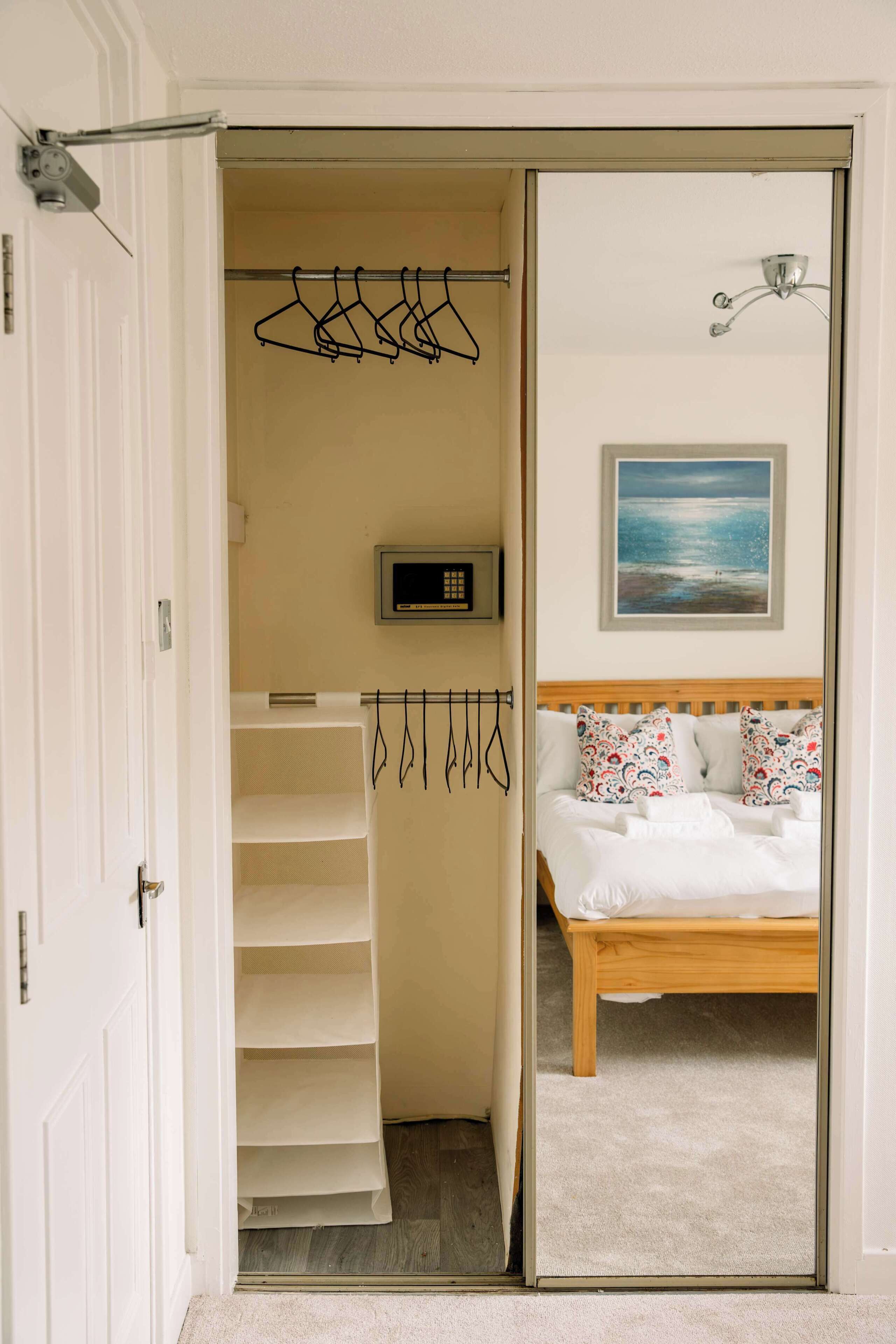 A bedroom with a bed, a painting, a digital clock, and a clothing rack.