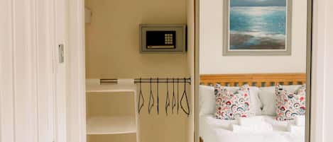 A bedroom with a bed, a painting, a digital clock, and a clothing rack.