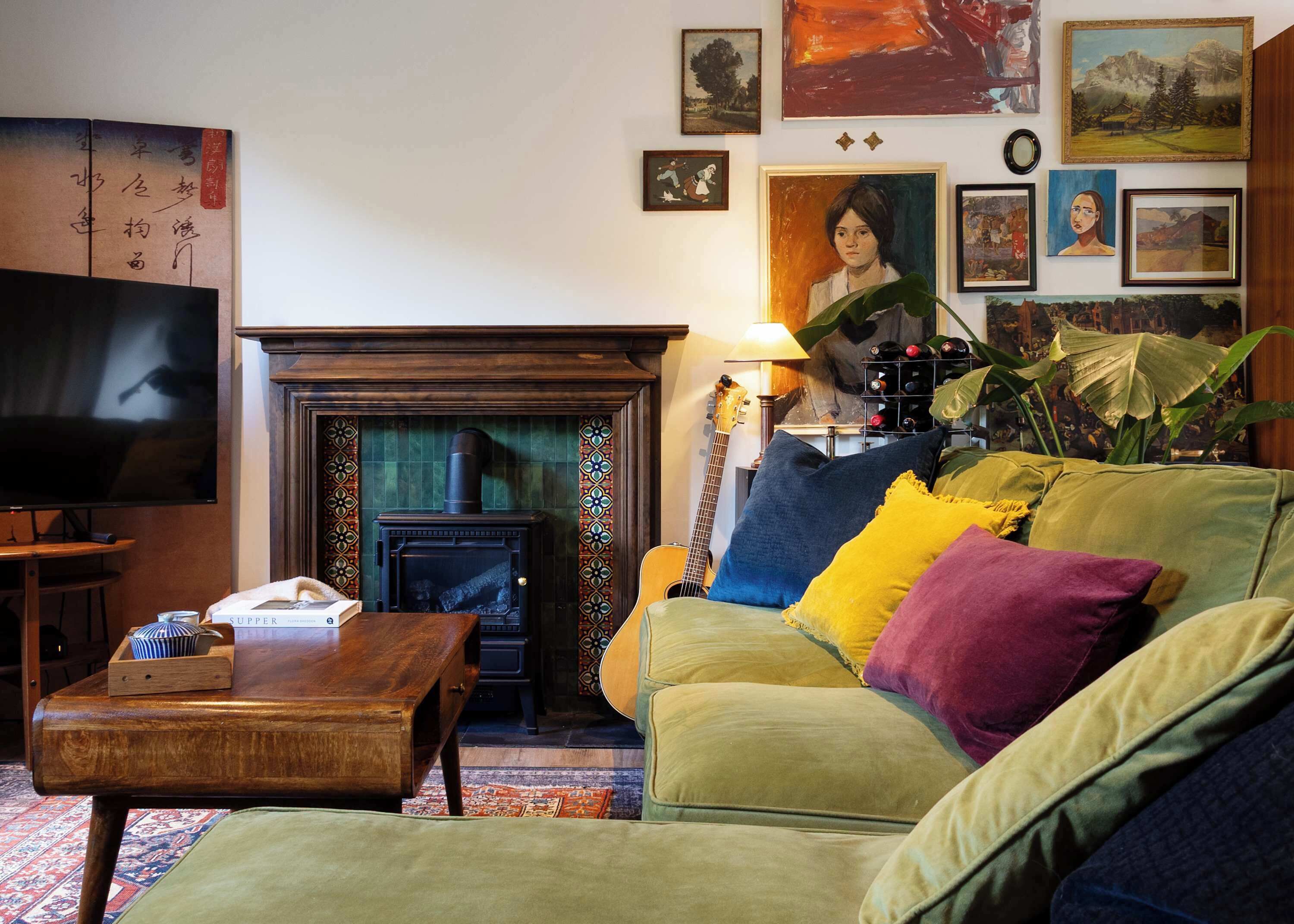 A cozy living room with a fireplace, a television, and various artworks on the walls.