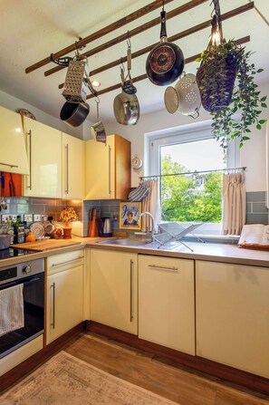 A kitchen with hanging pots, a window with a view, and a clock on the wall. - River View Home in Stockbridge with Parking and Study (Edinburgh)