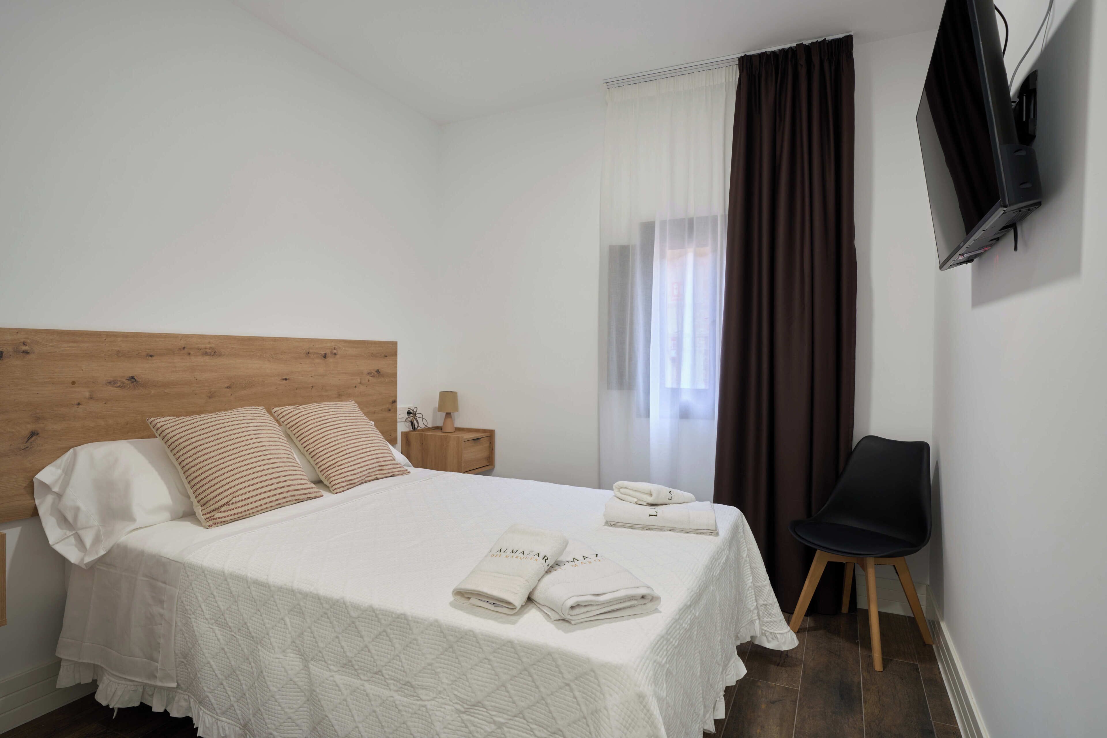 Een opgemaakt bed met kussens, een bedlampje en opgevouwen handdoeken op een witte laken.