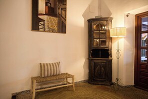 Una habitación de esquina con un banco, un armario alto, una lámpara de pie y un espejo en la pared.