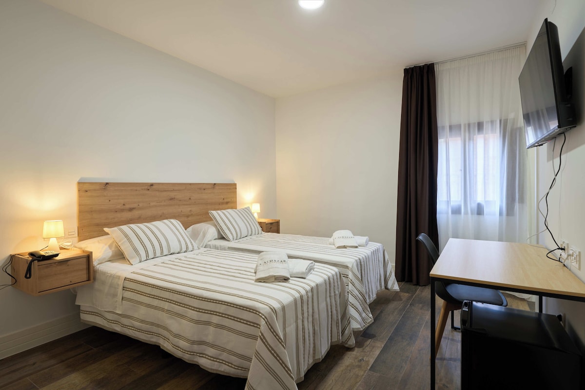 Una habitación de hotel con dos camas, un escritorio, un televisor y un teléfono en la mesita de noche.