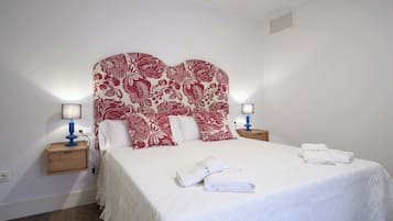 Een hotelkamer met een groot bed, twee nachtkastjes met lampen, een hoofdeinde met bloemenprint en een witte handdoek op het bed.