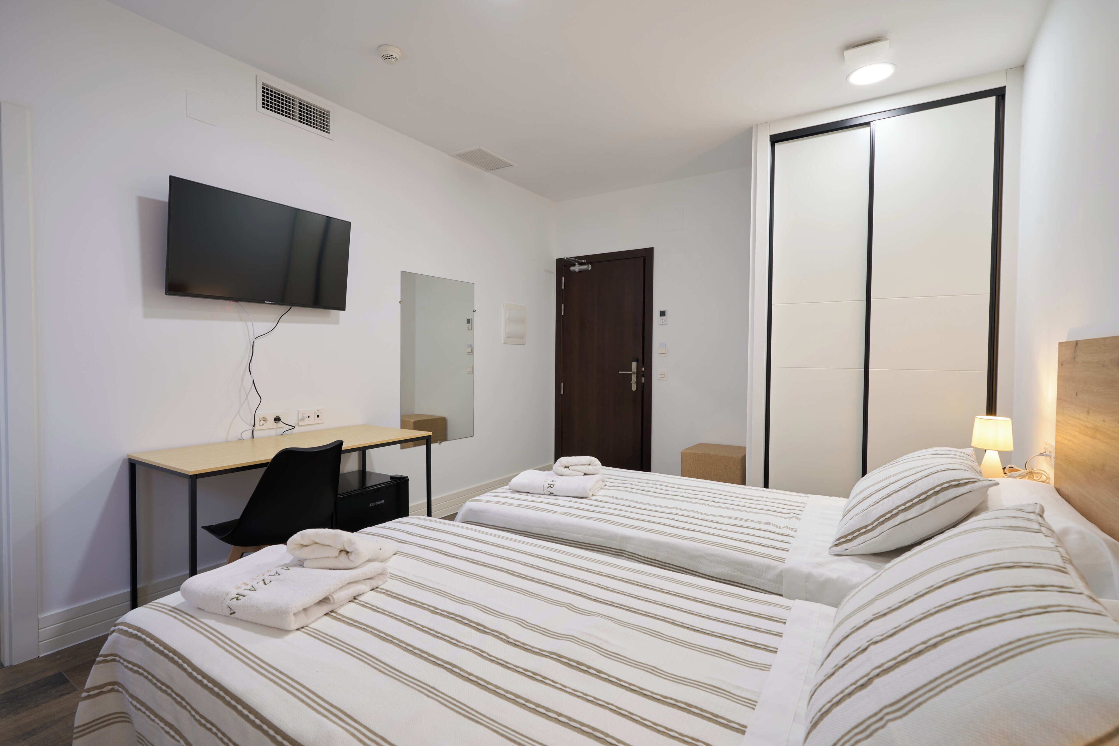Una habitació d'hotel amb dos llits, un escriptori, una televisió i un armari.