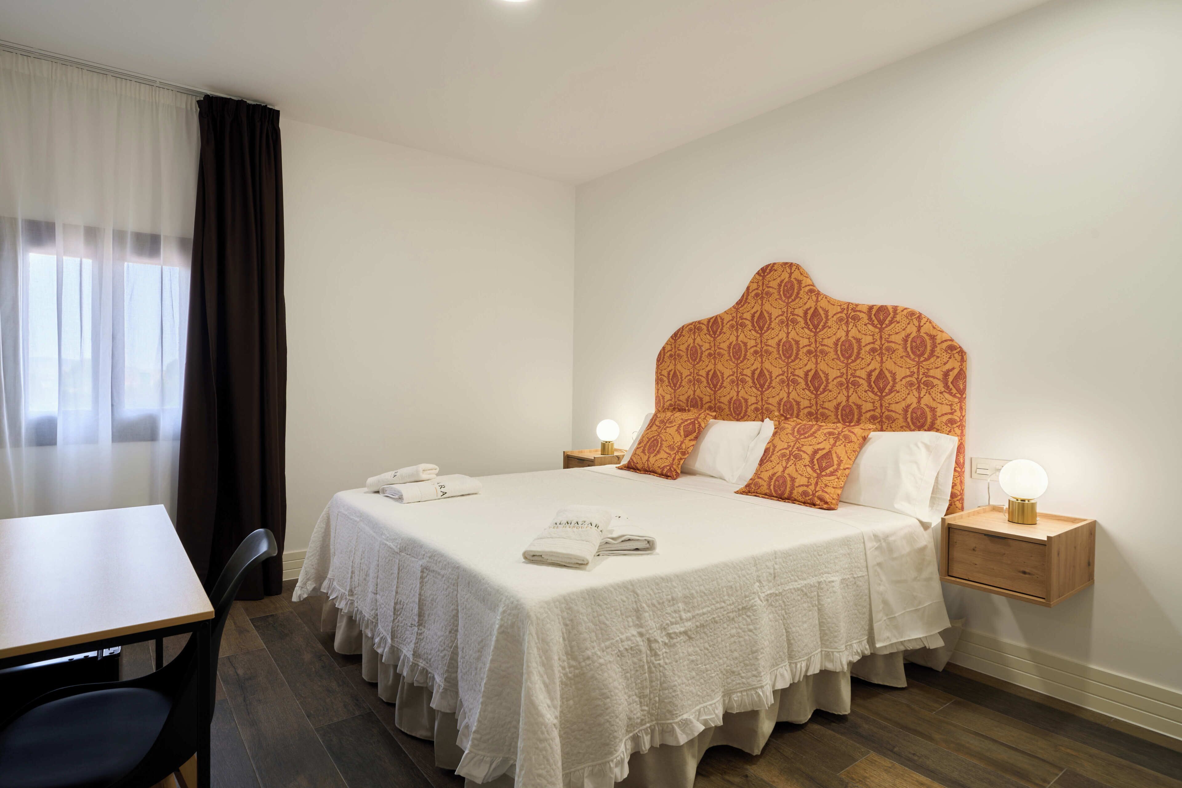A hotel room with a large bed, two bedside tables with lamps, a desk, and a chair.