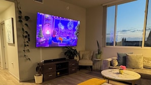Un salón moderno con un televisor de pantalla plana, un sofá, una mesa de centro y vistas a través de un ventanal grande.