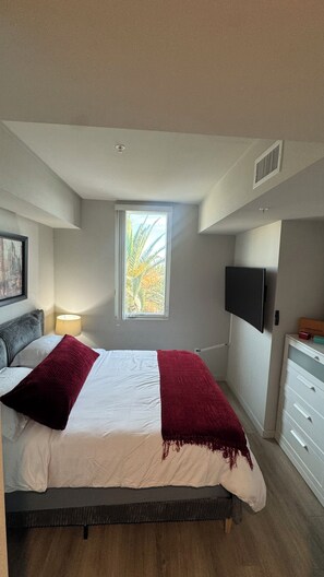 A bedroom with a bed, a window with a view, a mounted TV, and a bedside lamp.