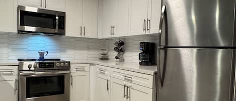 A modern kitchen with white cabinets, stainless steel appliances, and a wooden floor.