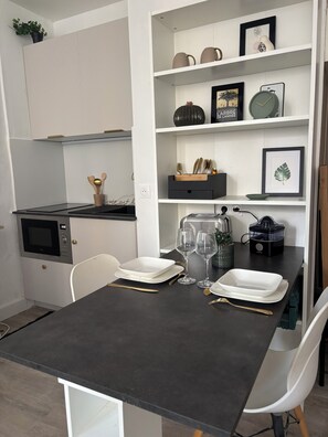 Uma cozinha moderna com armários brancos, bancada preta e um espaço de jantar com cadeiras brancas e mesa preta.