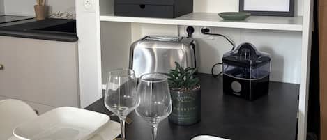 Una cocina con encimera negra, armarios blancos, un tostador, una licuadora y una planta en maceta.