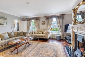 Een klassieke woonkamer met een bank, fauteuil en een open haard.
