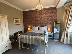 A bedroom with a bed, bedside lamps, a dresser, a mirror, and a chandelier.