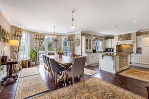 Een ruime keuken met moderne apparatuur, een eetgedeelte met een grote tafel en stoelen, en een zithoek met een bank en decoratieve objecten.