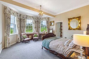 Een slaapkamer met een bed, een stoel, een bureau, een spiegel en een kroonluchter.