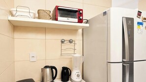 A kitchen with a red Oster toaster oven, a white refrigerator, a black kettle, a white blender, and a metal drying rack. - Lorenzo di Credi - LikeHome  (João Pessoa)