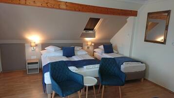 Une chambre avec deux lits, une petite table et deux chaises. Il y a une lucarne au-dessus des lits et un miroir sur le mur.
