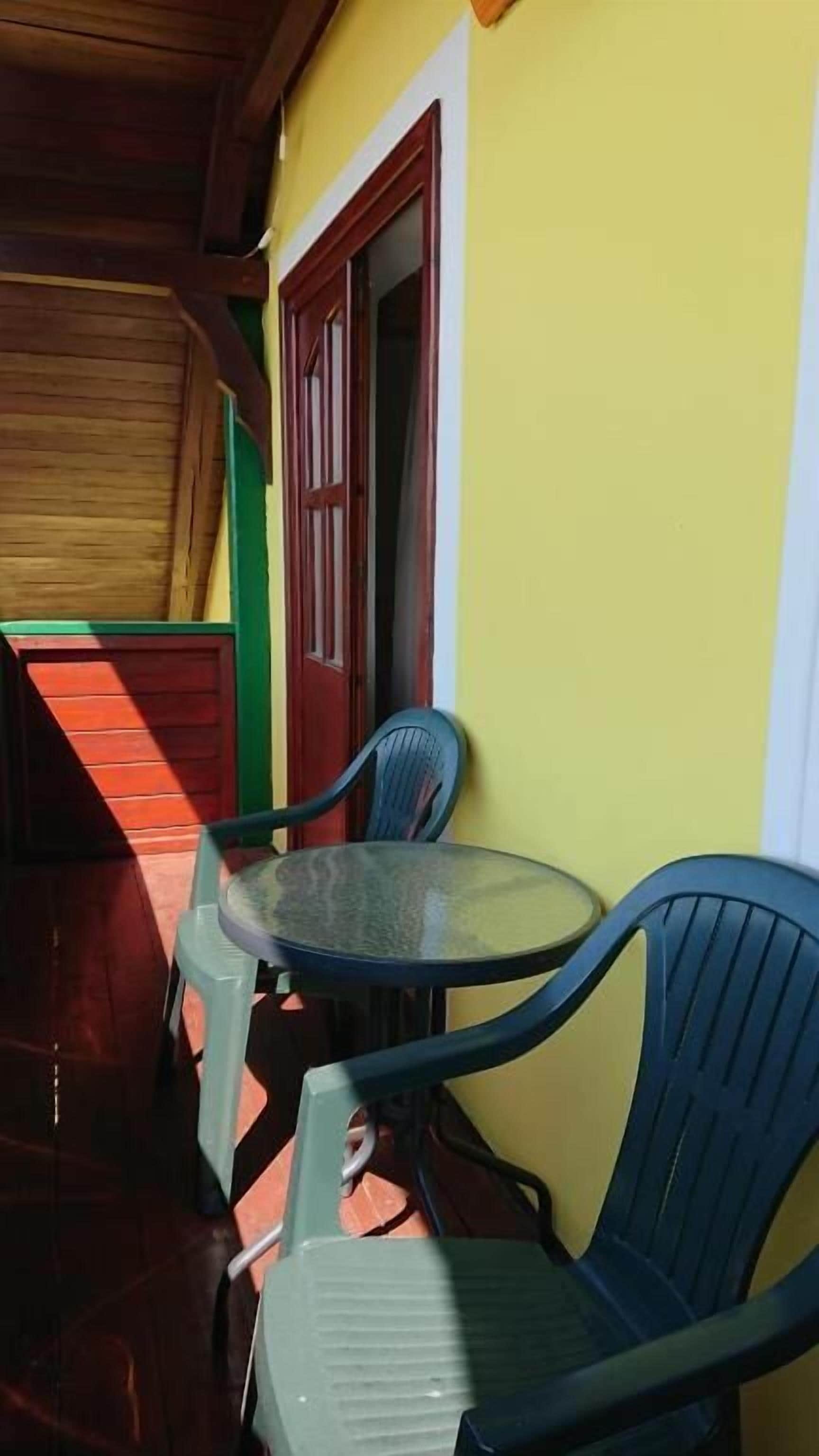 Un espacio de estar al aire libre techado, con una mesa redonda y dos sillas, techo de madera y una puerta con marco rojo.