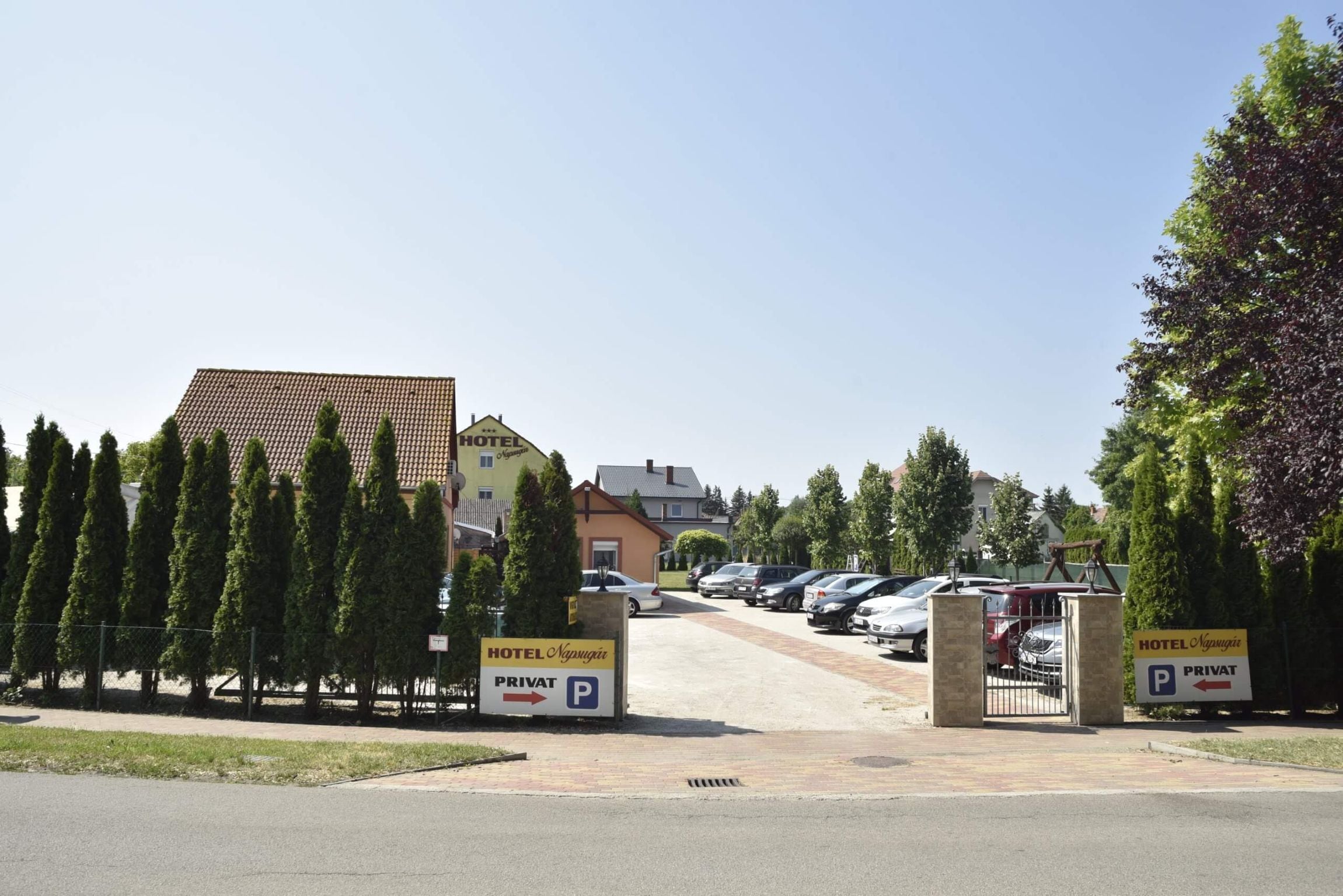 Entrada de um hotel com área de estacionamento, placa indicando estacionamento privado e uma fileira de carros estacionados.