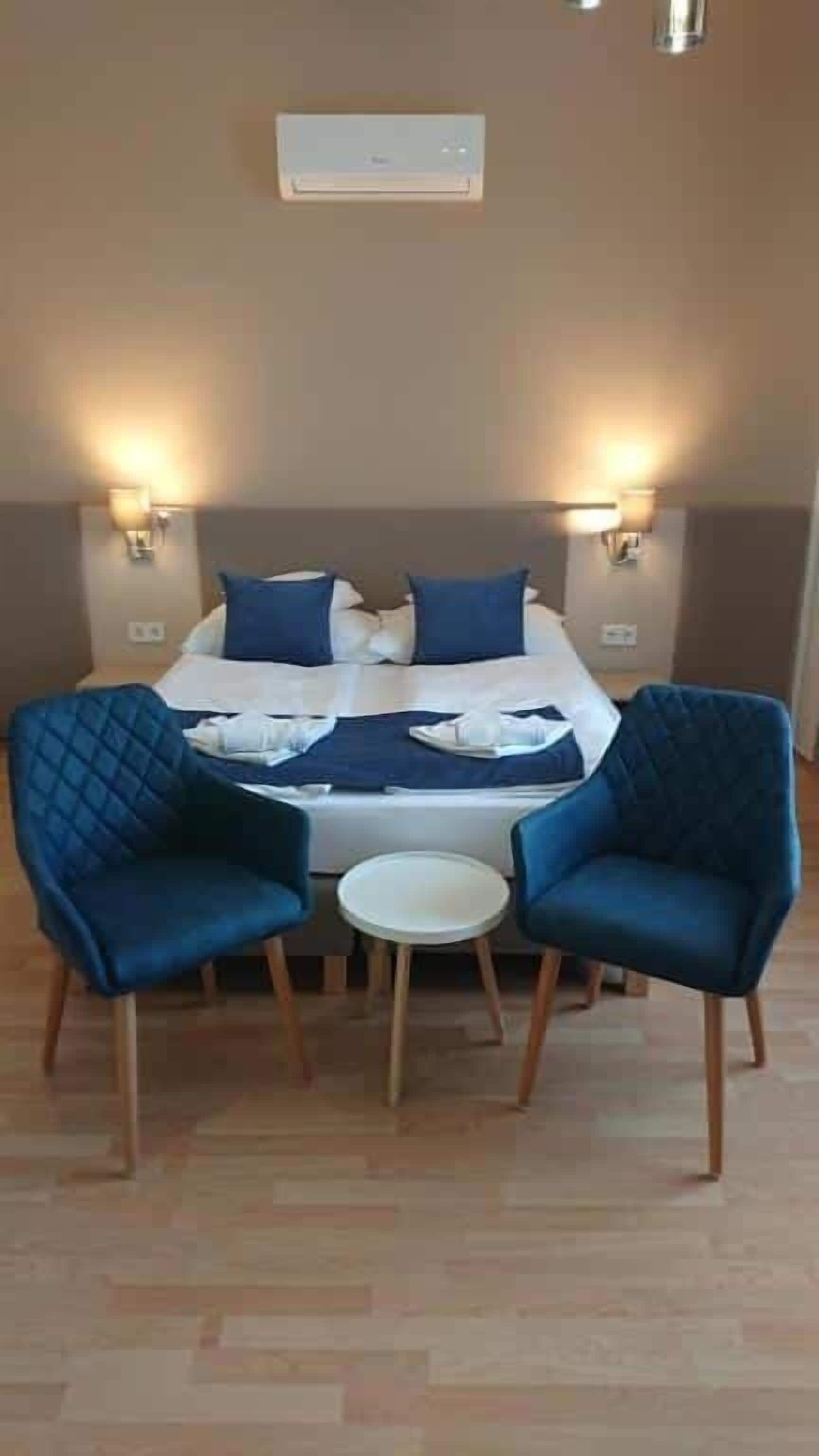 Et hotelværelse med en seng, to stole, et lille bord og vægmonterede lamper.