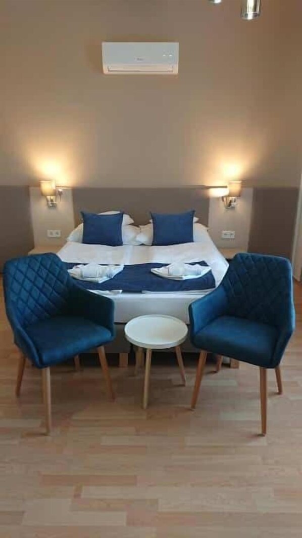 A hotel room with a bed, two chairs, a small table, and wall-mounted lights.