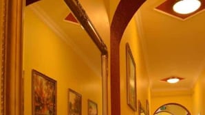 Un pasillo con paredes amarillas, detalles en rojo y suelo de baldosas. Se observan cuadros enmarcados en las paredes y un espejo grande a la izquierda.