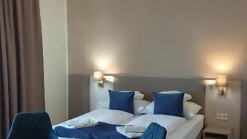 A hotel room with a bed, bedside tables, a chair, a small table, and a hanging light fixture.