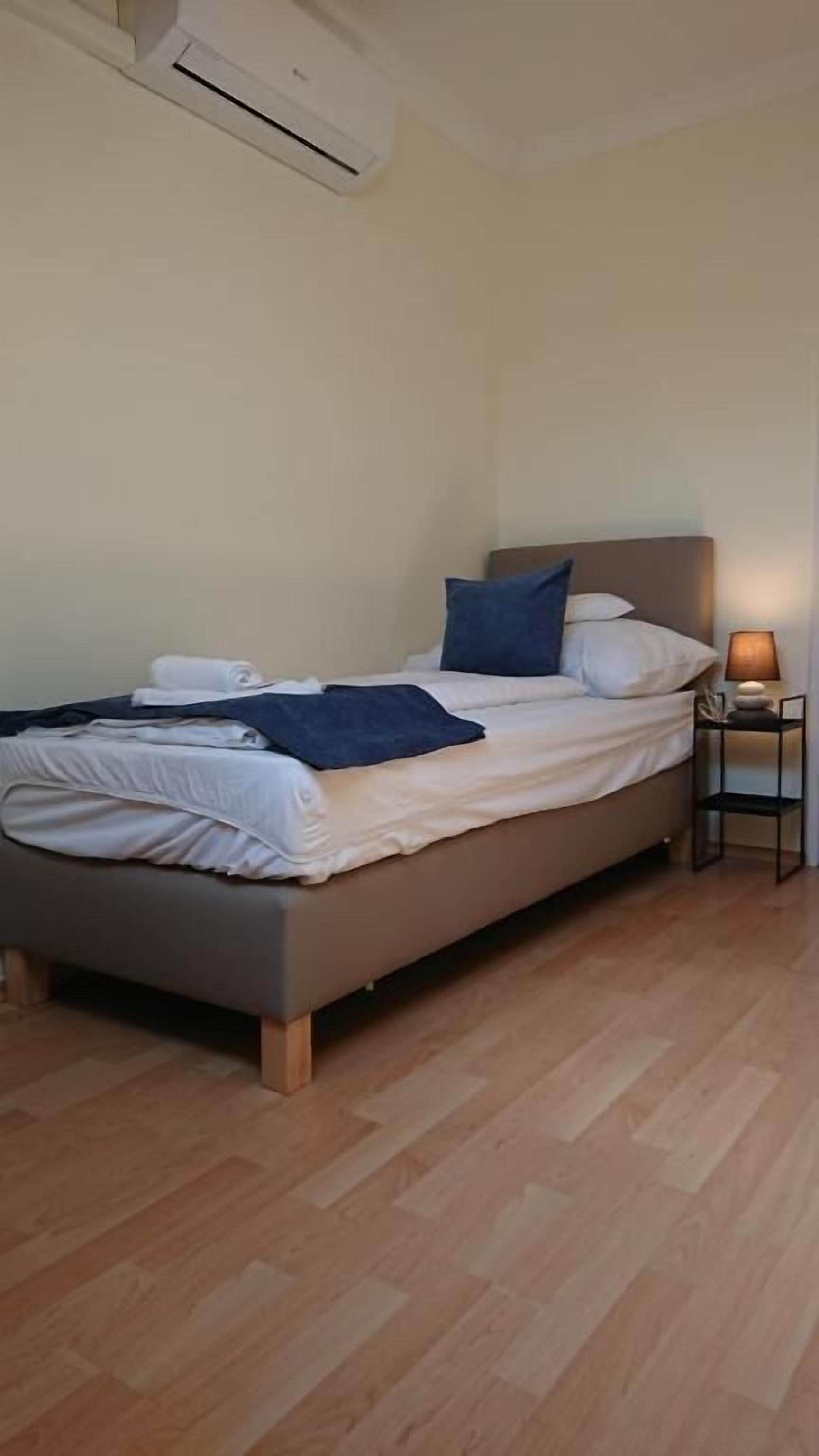 A single bed with a headboard, a bedside table with a lamp, and a wooden floor.
